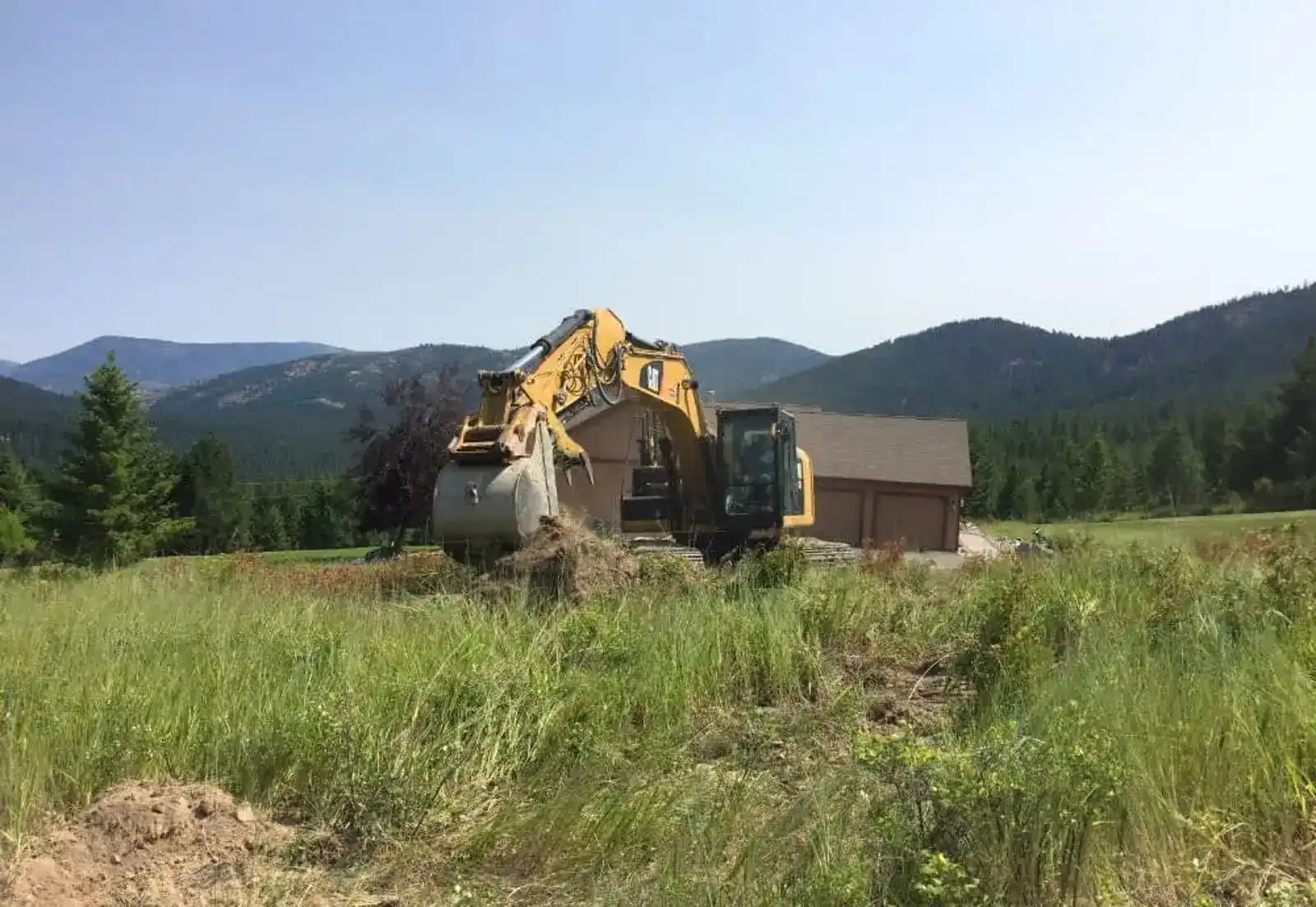 Excavator on a cleared building site below the Montana mountains