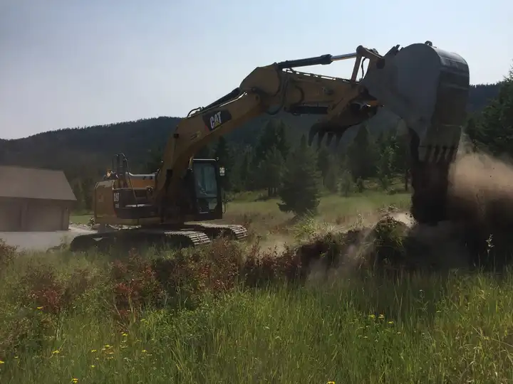 Excavator grading a site below the hills, dust in the air